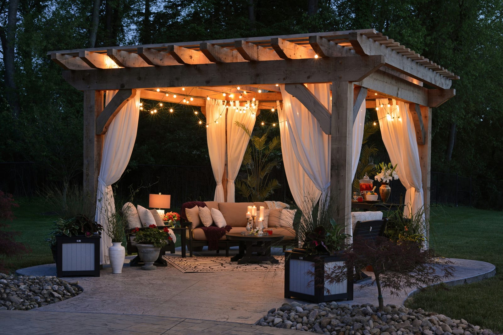 Evening pergola with string lights and curtains over a stone patio lounge